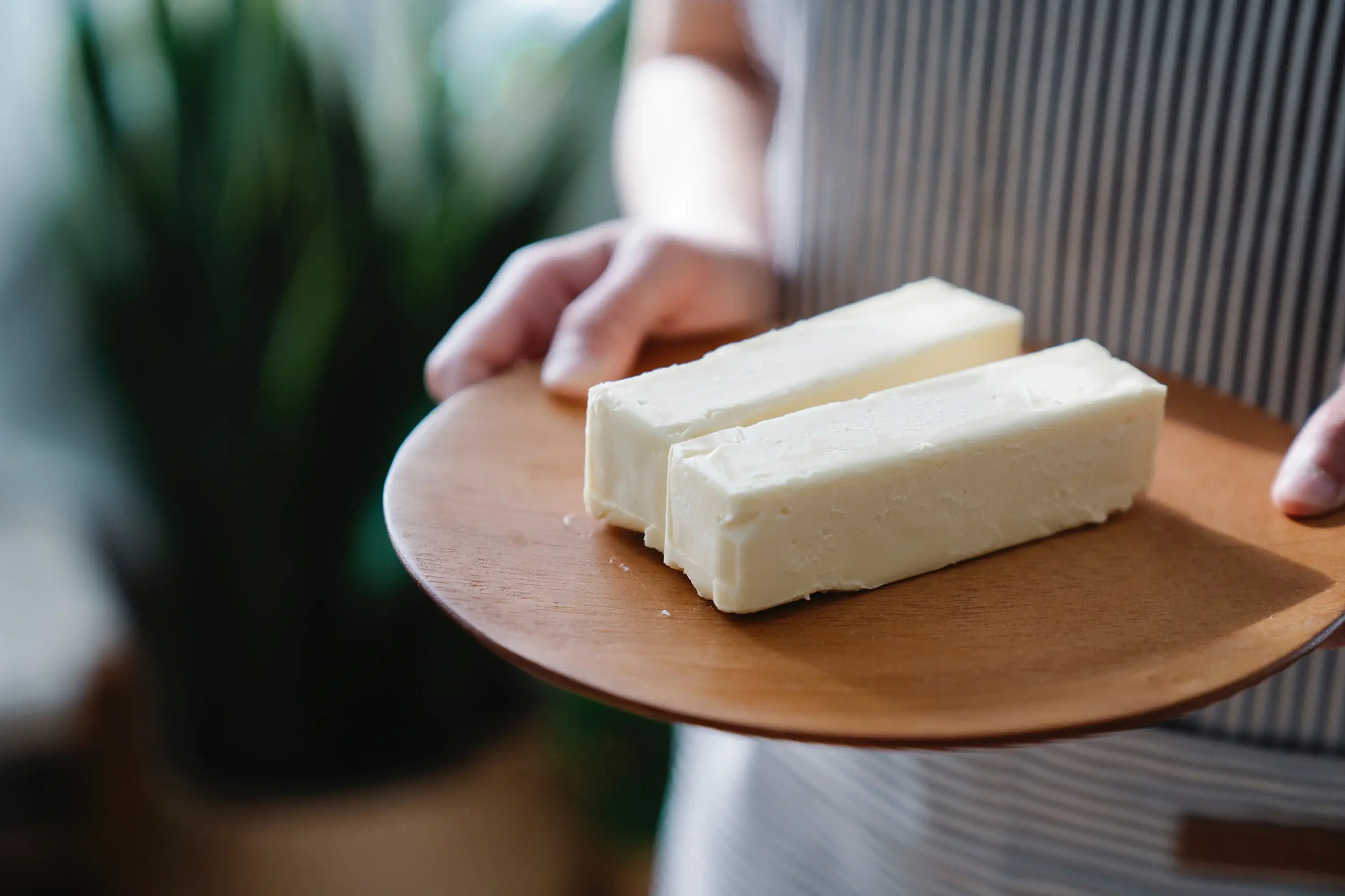 person holding two sticks of butter on a wooden serving plate